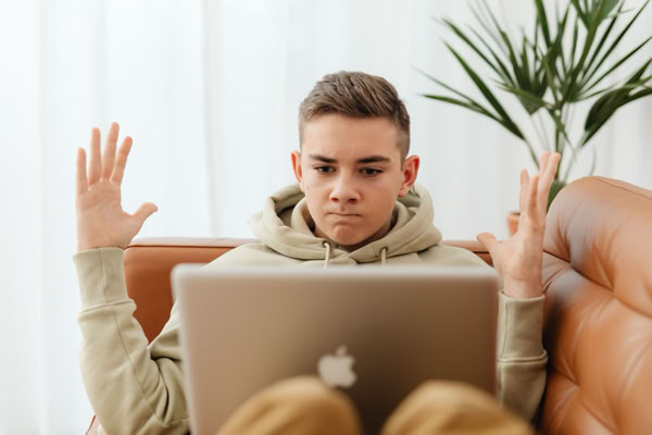 A person sitting on a couch with a laptop on their lap, raising their hands, with a plant in the background.